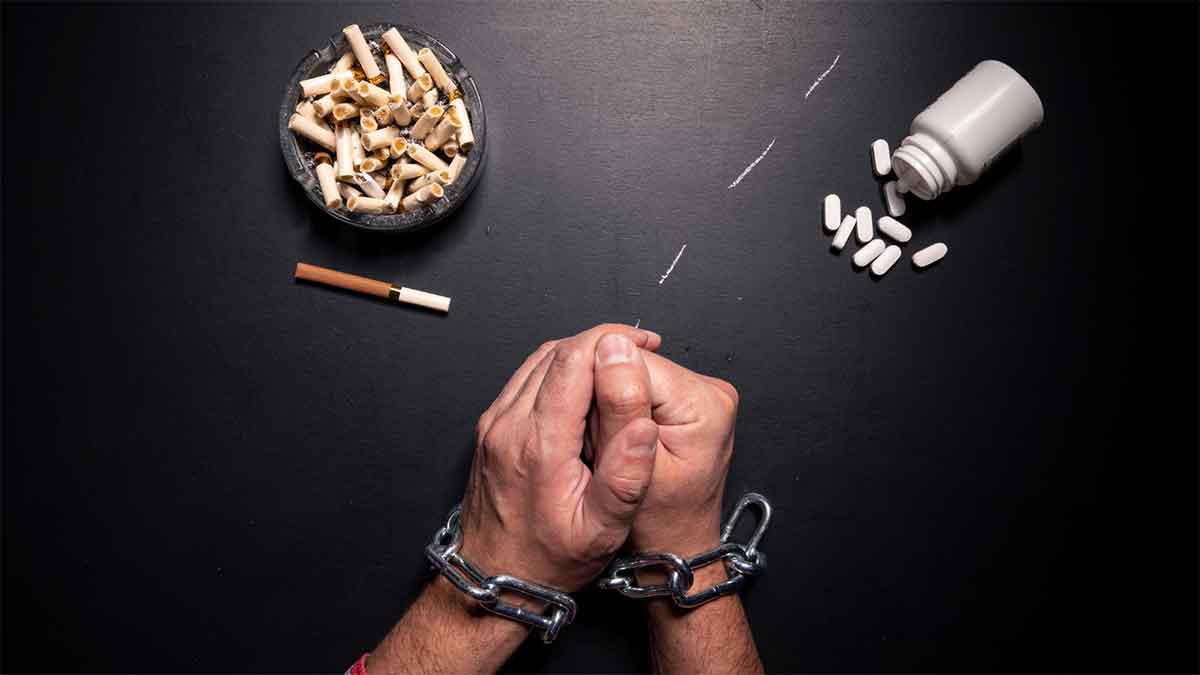 Hands in chains, surrounded by cigarettes, pills, and drugs.