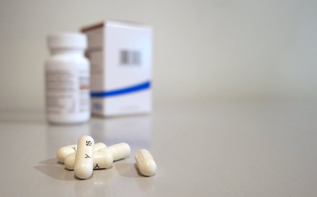 A close-up of white capsules labeled "Y 15" scattered on a surface, with a pill bottle and box in the background.