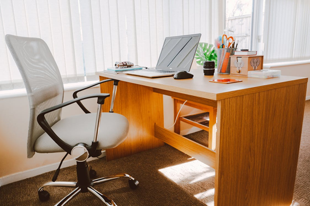 Well-lit home office setup with an ergonomic chair, laptop on a wooden desk, and office supplies, ideal for focused work