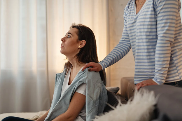 Woman receiving supportive shoulder touch from another in a calming room, conveying comfort and understanding.