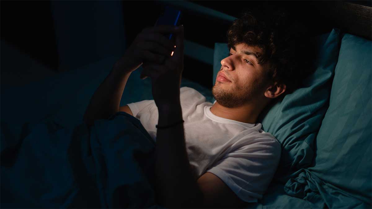 A man scrolling through his phone while laying down on his bed