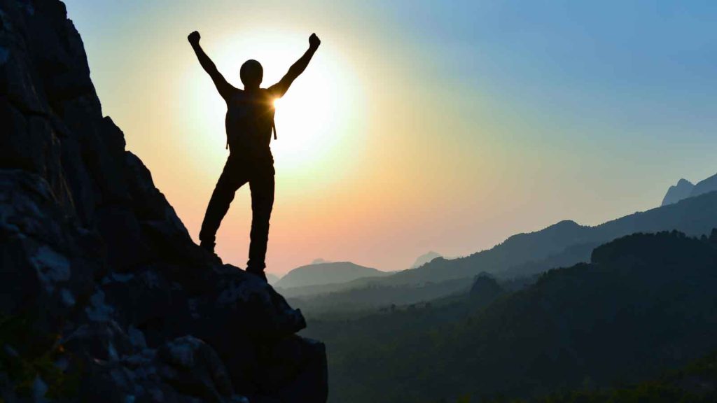 A hiker celebrating at the summit during sunrise