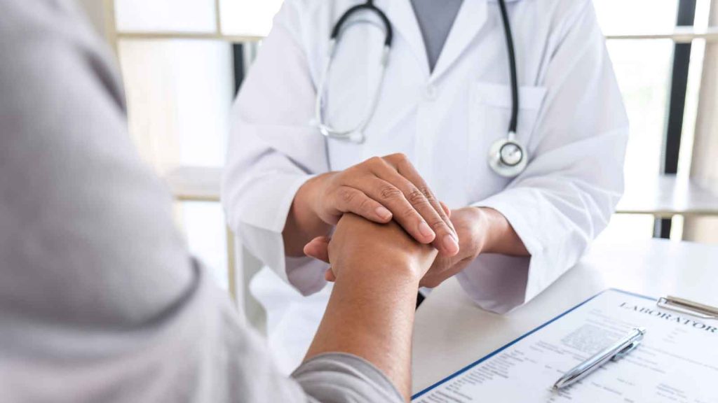 Doctor holding a patient's hand during a reassuring conversation.