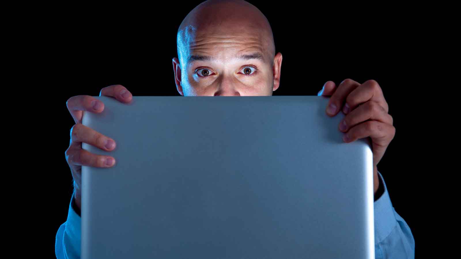 Man looking shocked while staring at a laptop screen in the dark.