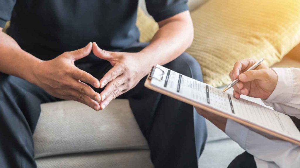 Person in therapy session speaking to a professional with a clipboard
