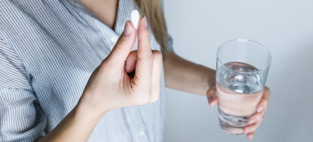 A person holding a pill and a glass of water