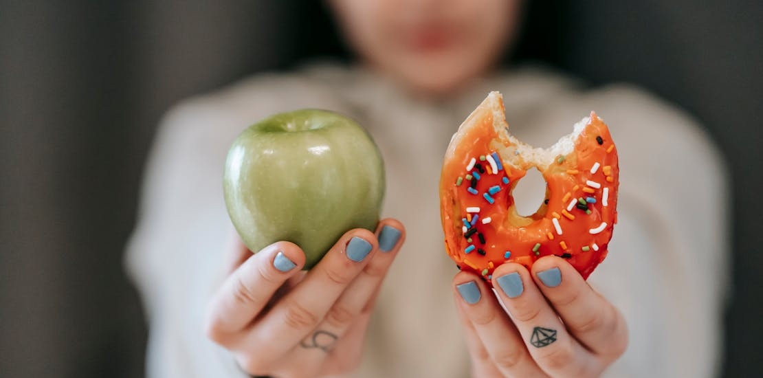a person holding an apple and a doughnut