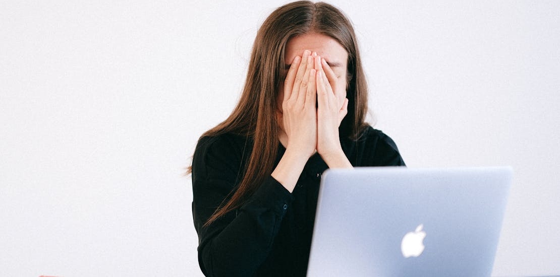 woman with hands on her face in front of a laptop