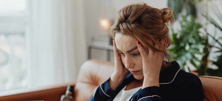 A person sitting on a couch, holding their head.